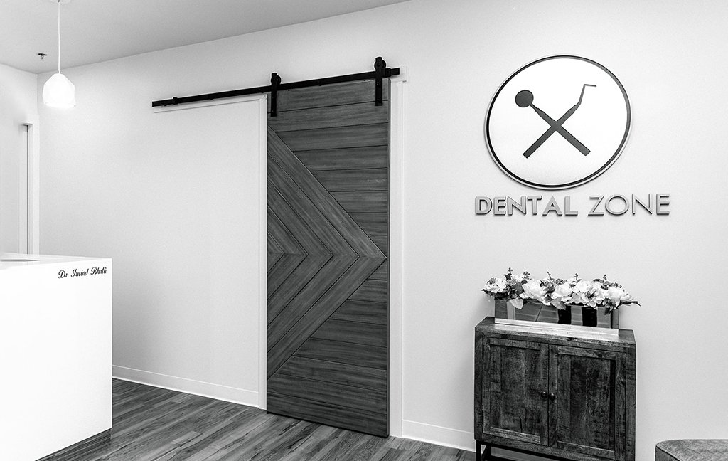 Black and white view of the Dental Zone logo sign, a wooden barn door and the front desk.