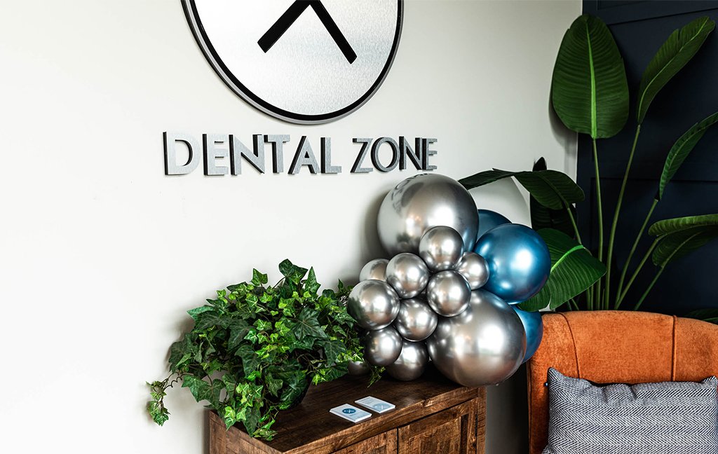Dental Zone wall sign above a wooden cabinet with silver and blue balloons, plants and an orange chair.