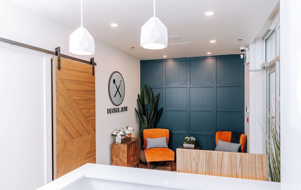 Waiting area with two orange chairs, a dark blue paneled wall, a sliding barn door and the Dental Zone sign.